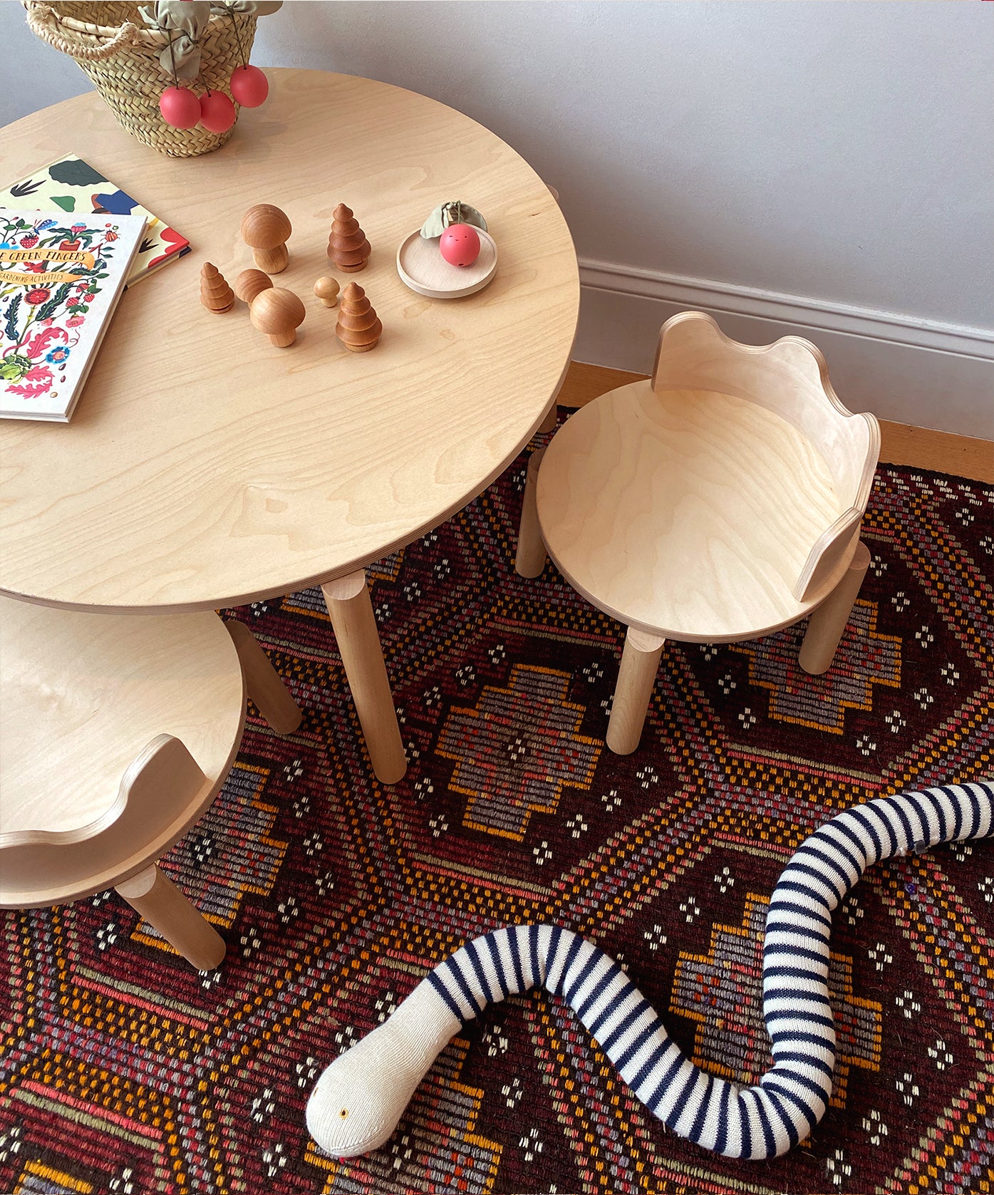 Moss Table with toys on it, children's wooden chairs, patterned rug, and a striped fabric snake on the floor.
