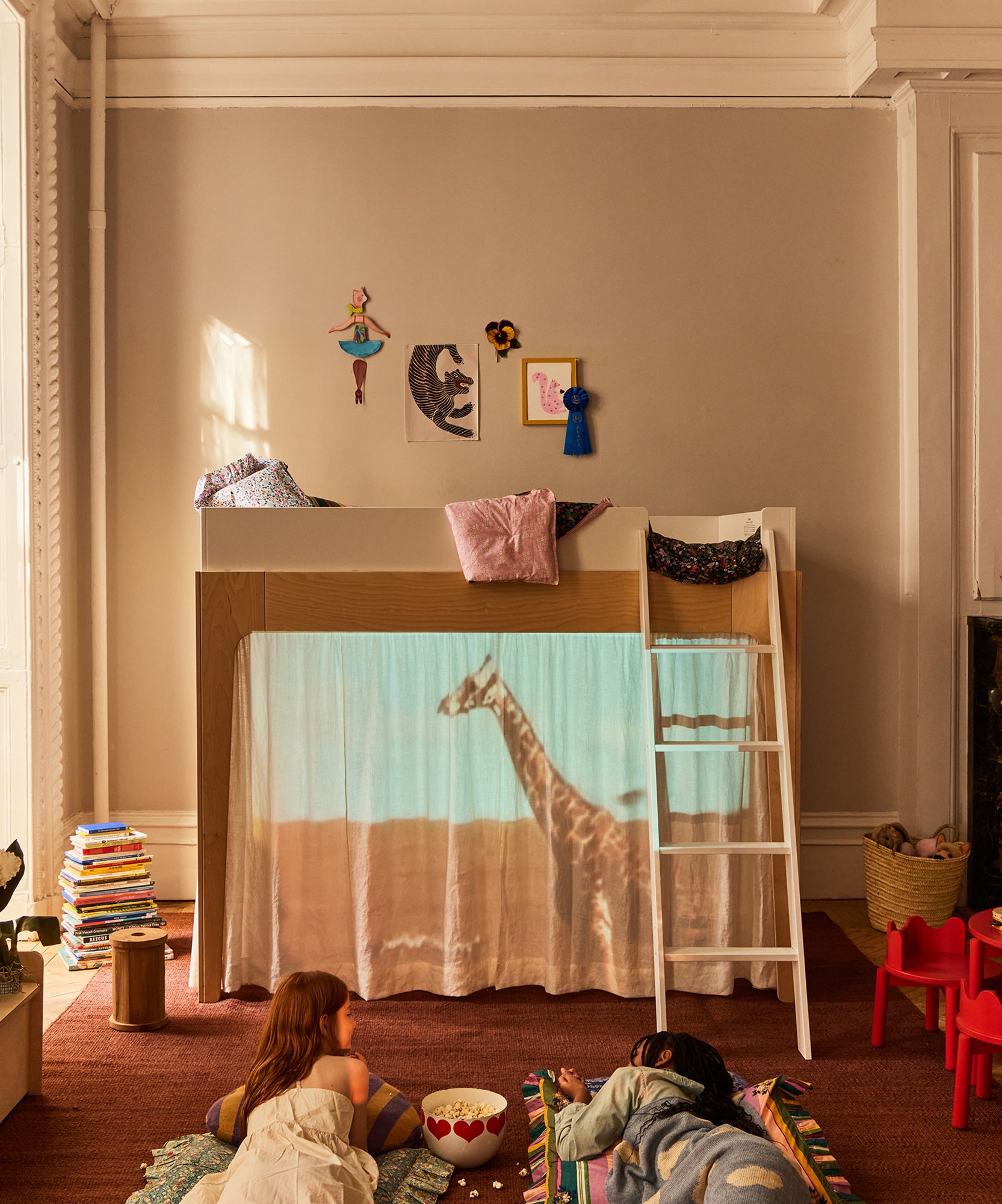 Two children watch a giraffe projected on the curtain of a Perch Full Loft Bed in a cozy, sunlit bedroom.