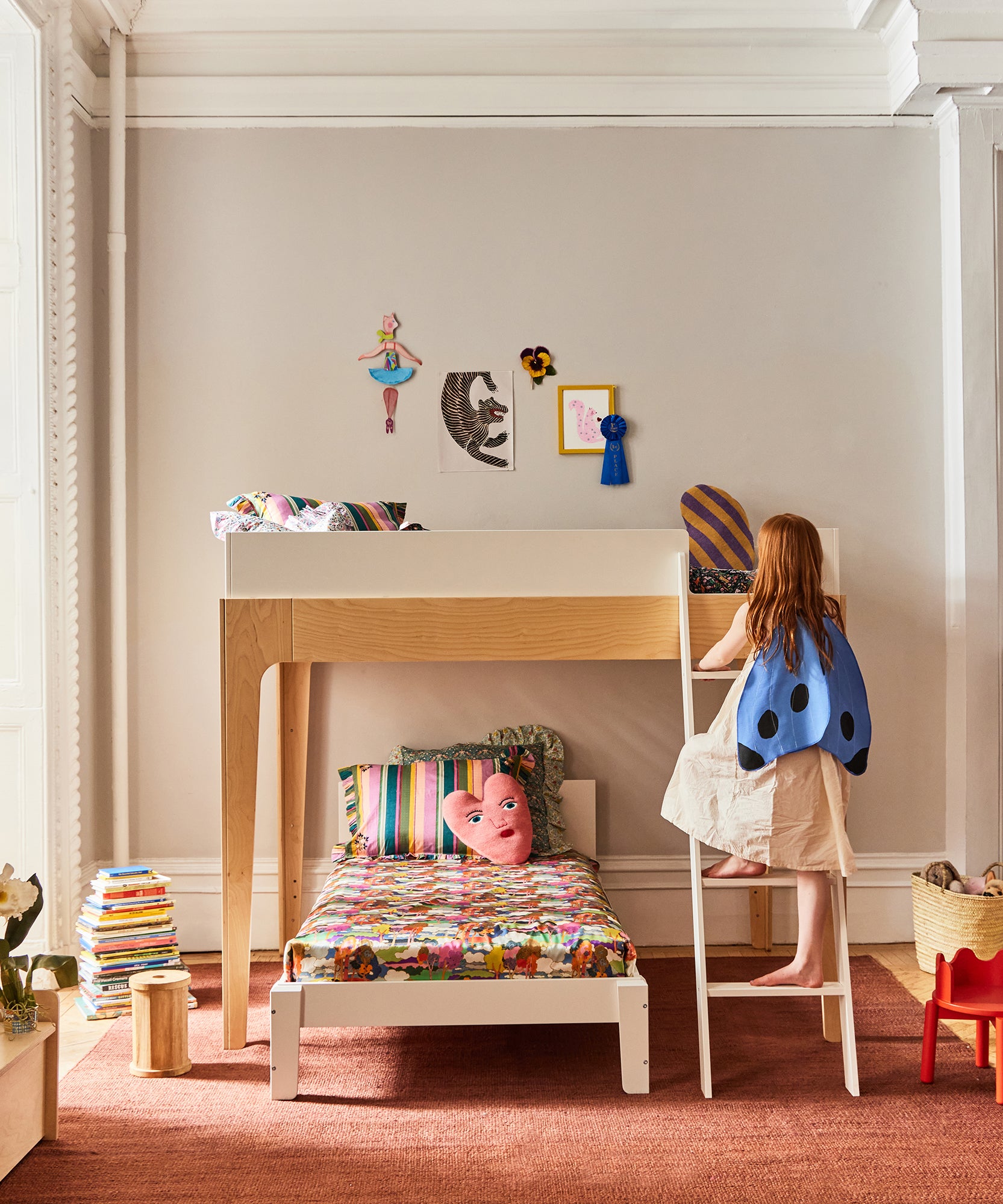 A child in a ladybug cape climbs the Perch Full Loft Bed in a colorful, cozy bedroom.
