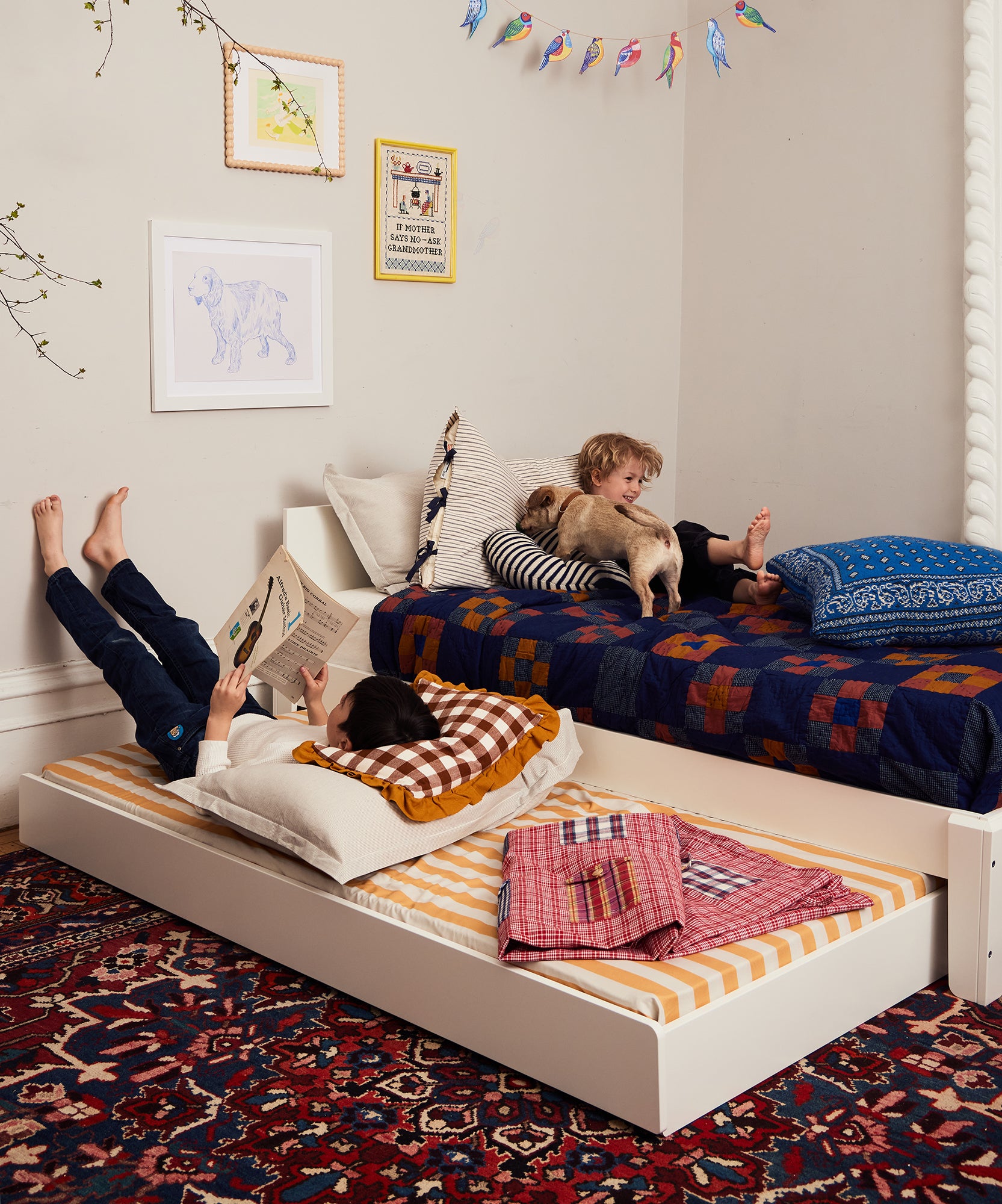 Two children relax on Perch Trundle Beds with the Ladder Conversion Kit; one reads, the other pets a dog in a cozy, colorful bedroom.