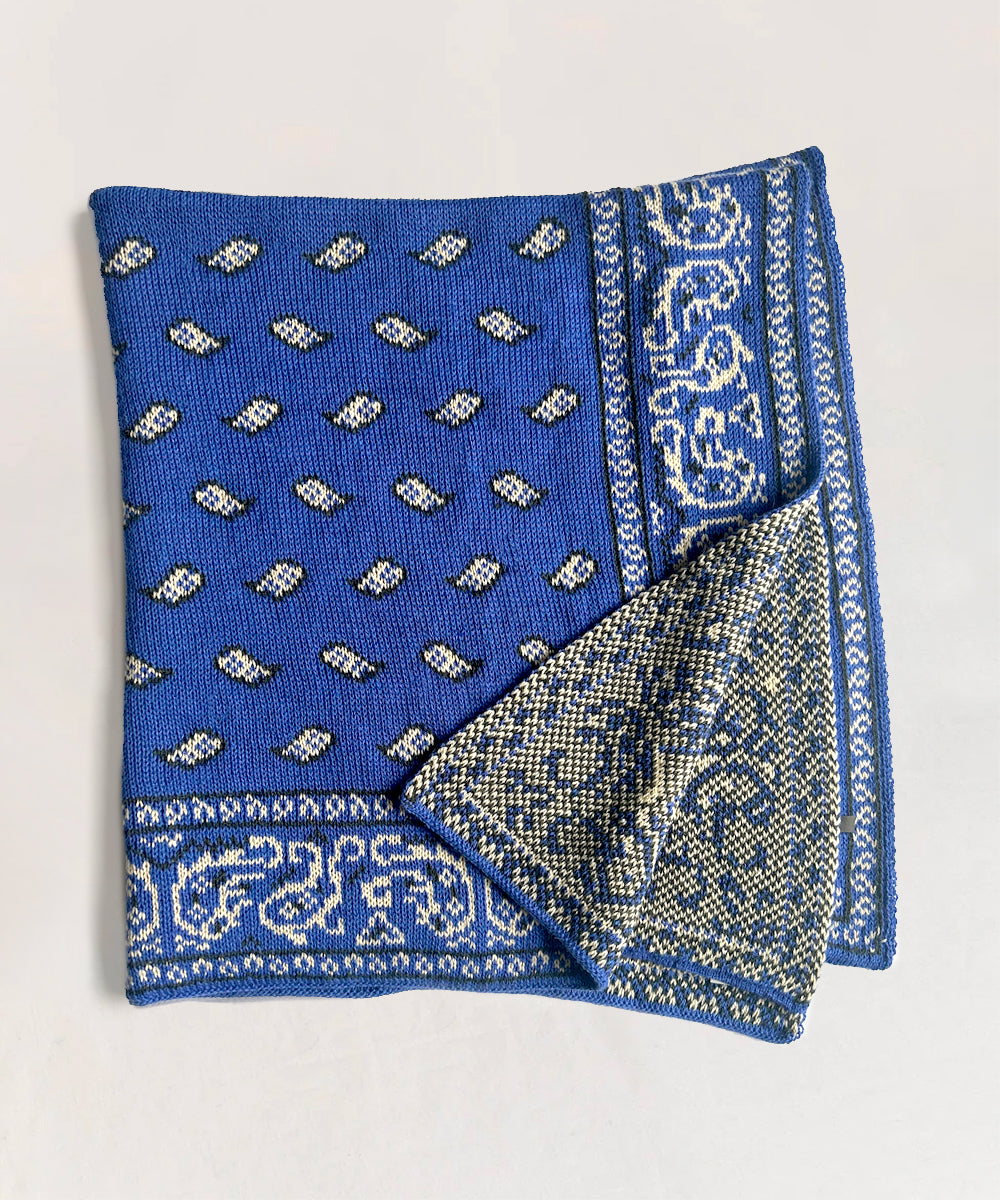A folded blue Bandana Blanket features white paisley patterns and an intricate border design on a light background.