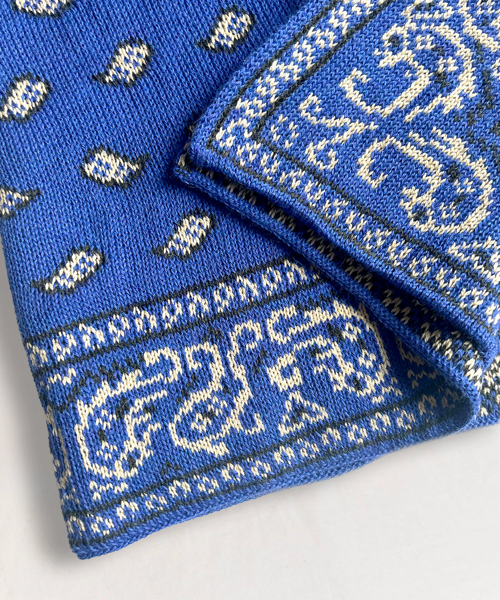 Close-up of a Bandana Blanket featuring folded blue knit fabric with white paisley and geometric patterns.