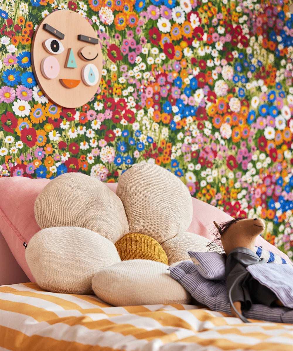 A child's bedroom features floral wallpaper, a wooden face on the wall, and a Daisy Pillow on the bed.