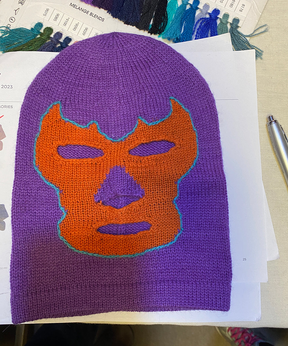 A purple knitted balaclava features an orange and teal luchador-style mask, named the Luchador Mask.
