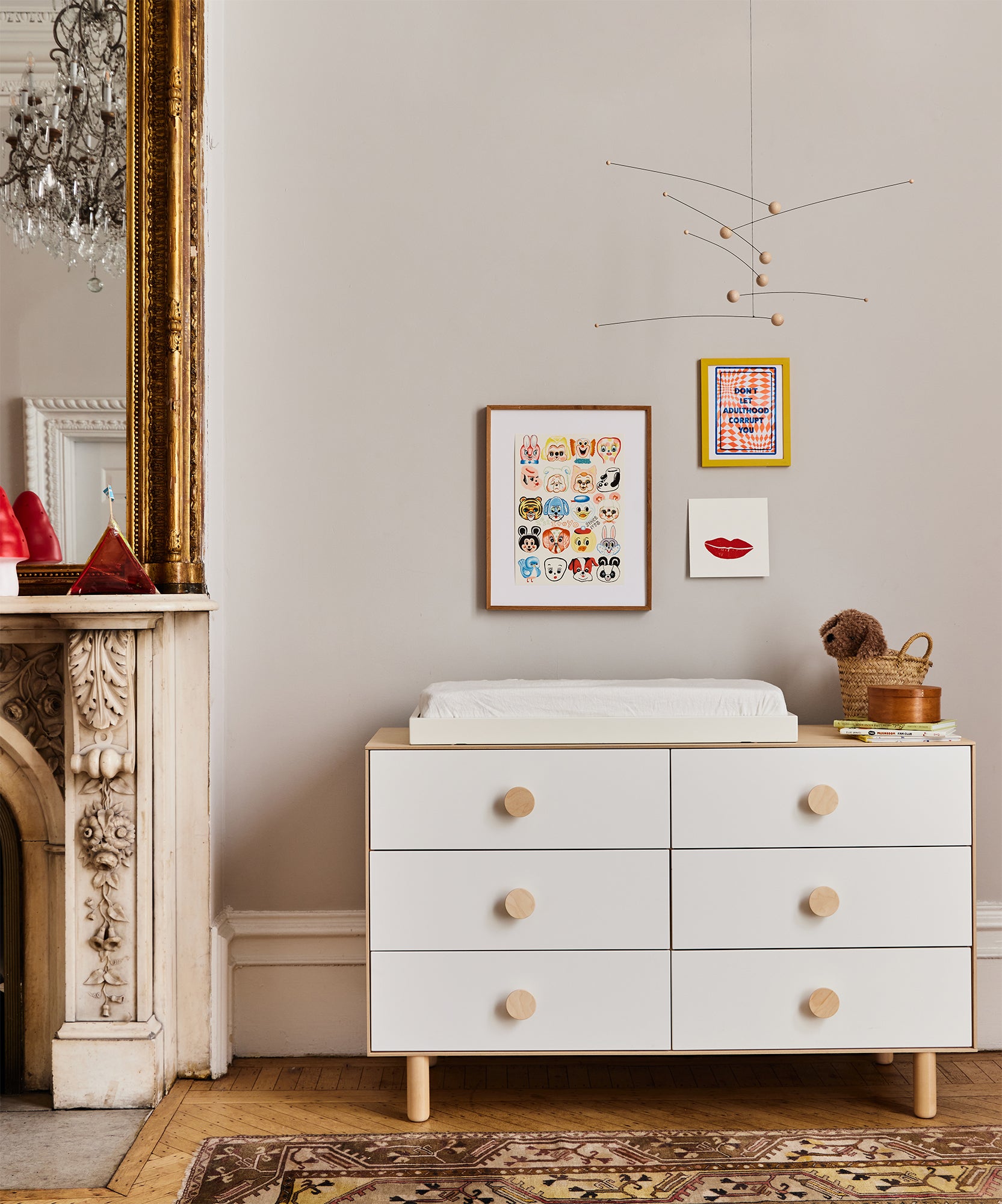 Dot 6-Drawer Dresser with changing pad, wall art above, and mobile; ornate mirror and fireplace beside.