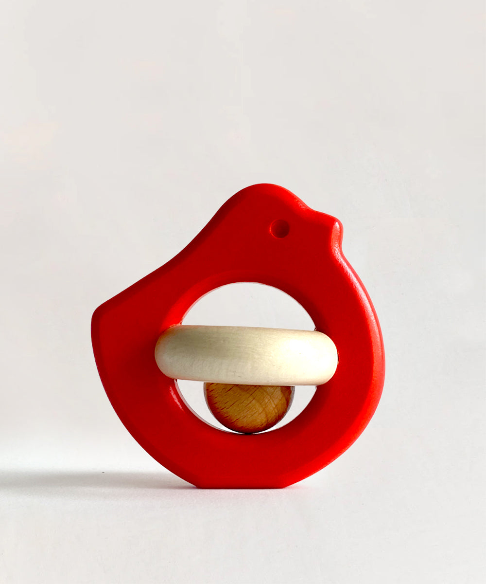 Le Baby Bird Rattle: a red, bird-shaped wooden rattle with a white ring and small wooden ball inside, shown on a plain background.