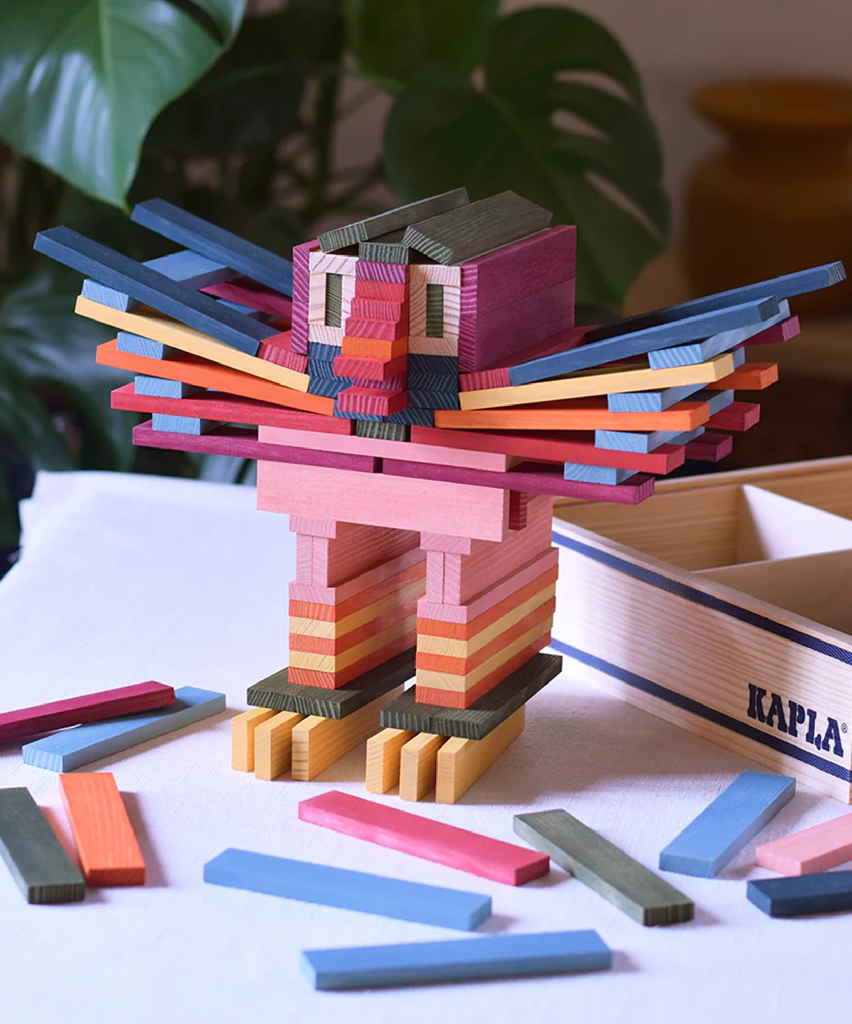 A colorful lion built from the KAPLA 100 Octocolor Case sits on a table, with extra wooden blocks scattered around.