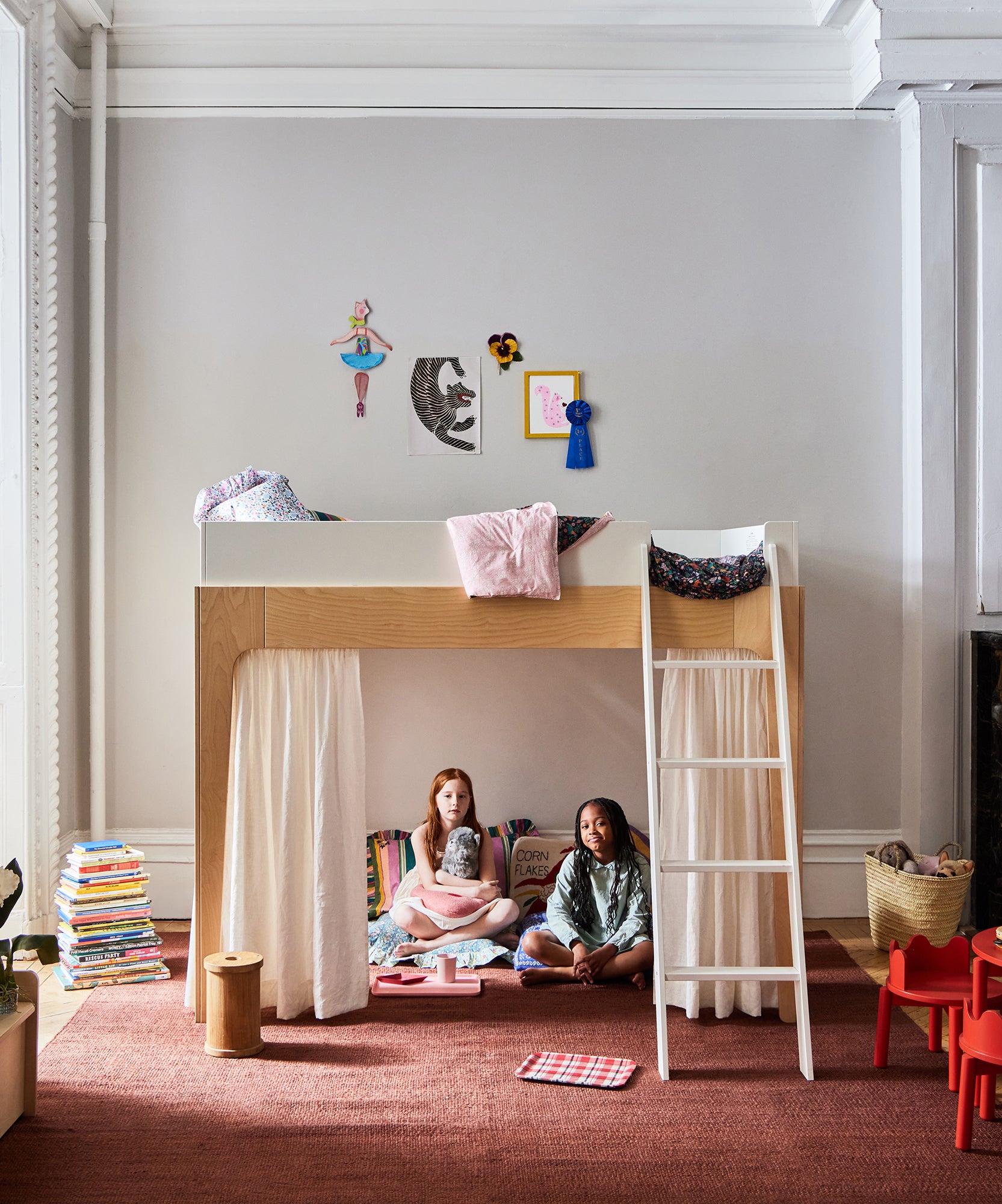 Two girls sit under a Perch Full Loft Bed in a cozy, decorated room filled with books, toys, and wall art.