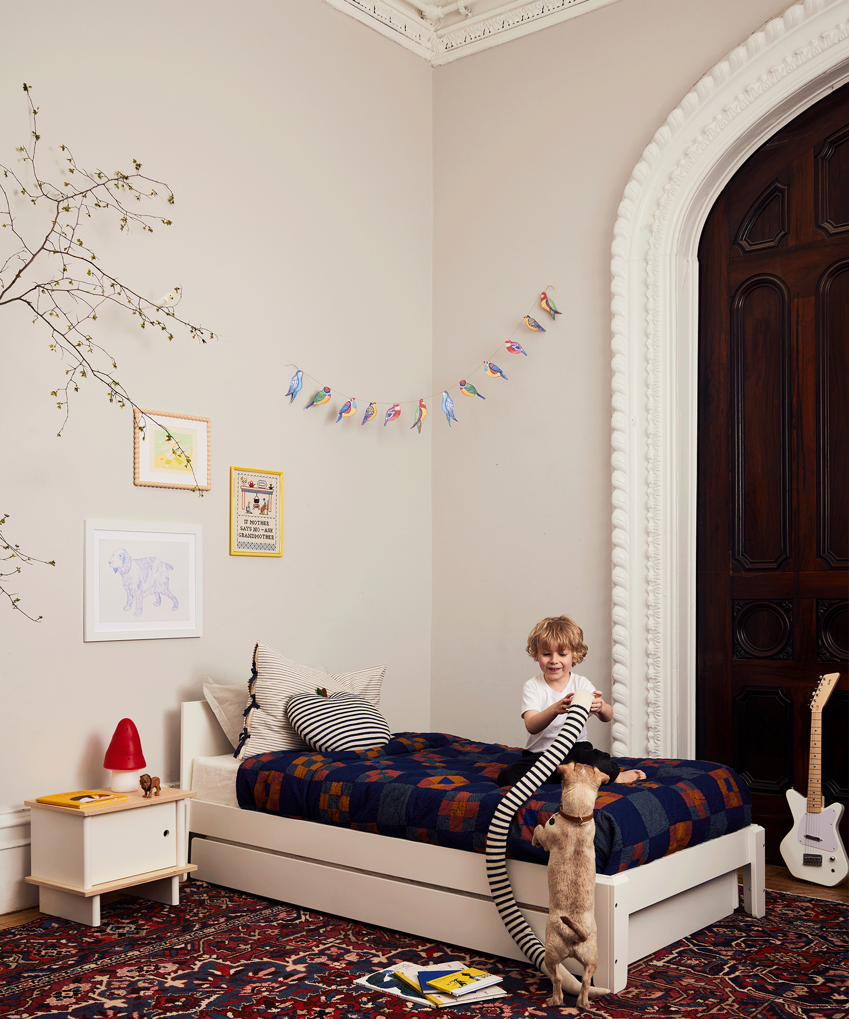 A young child plays with a cat beside a bed in a cozy, colorful bedroom, hugging a playful Snake Pillow.