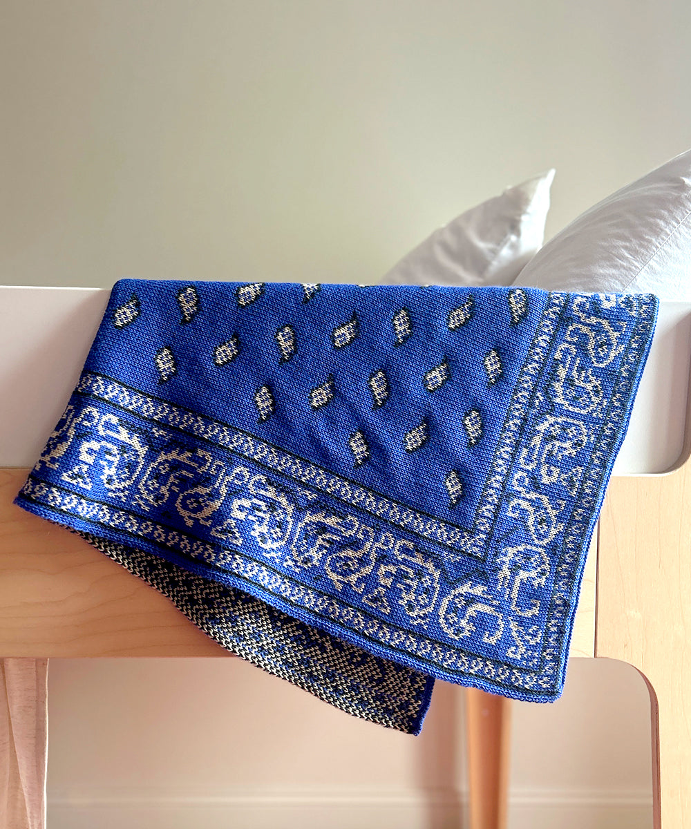 Bandana Blanket with geometric and leaf designs draped over a wooden chair with a pillow on it.