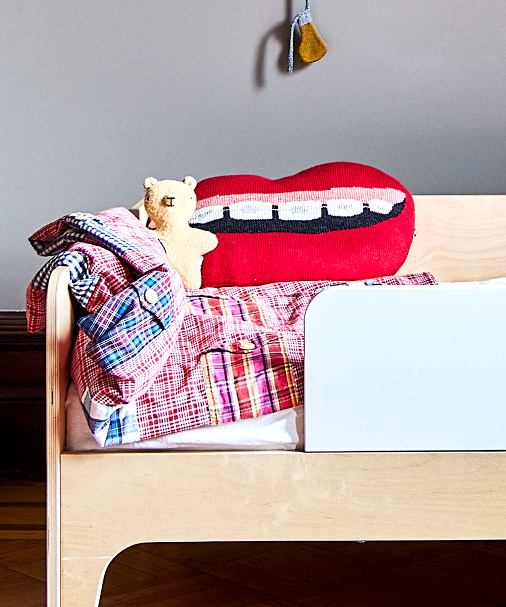 Children's bed with a checkered blanket, teddy bear, and a pillow called "Mouth Pillow - Braces.