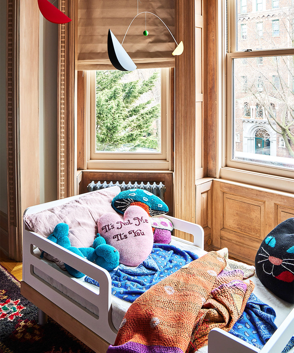 Cozy room featuring a Bandana Blanket on the child's bed, decorative pillows, and a colorful mobile by the window.