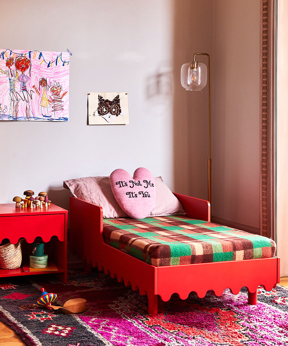 Childs room featuring a Moss toddler bed in red, heart pillow, colorful blanket, wall art, and toys on a rug.